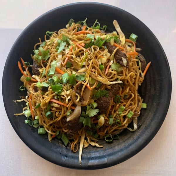 A black bowl filled with beef lo mein, garnished with green onions and cilantro.